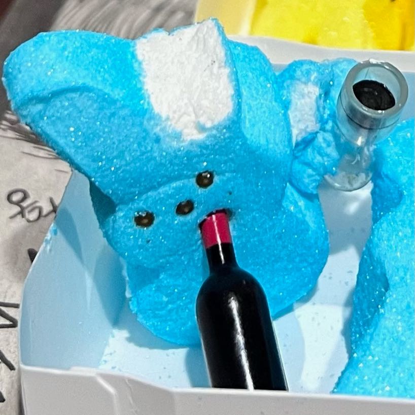 A blue rabbit Peep with a broken ear, a miniature wine glass and a miniature bottle in his mouth