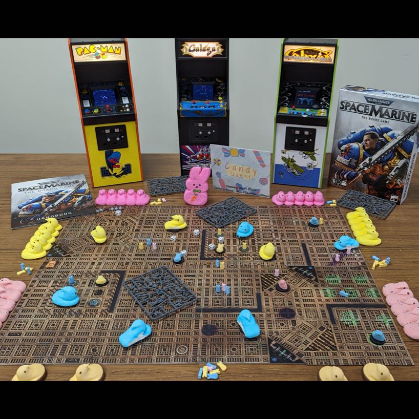 A large tabletop game board with Peeps arranged around it and miniature arcade games in the background